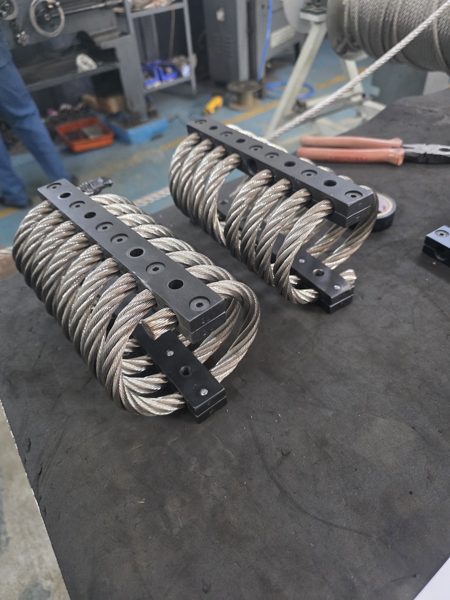 Two heavy AWRI wire rope isolators with black retainer bars on the assembly bench